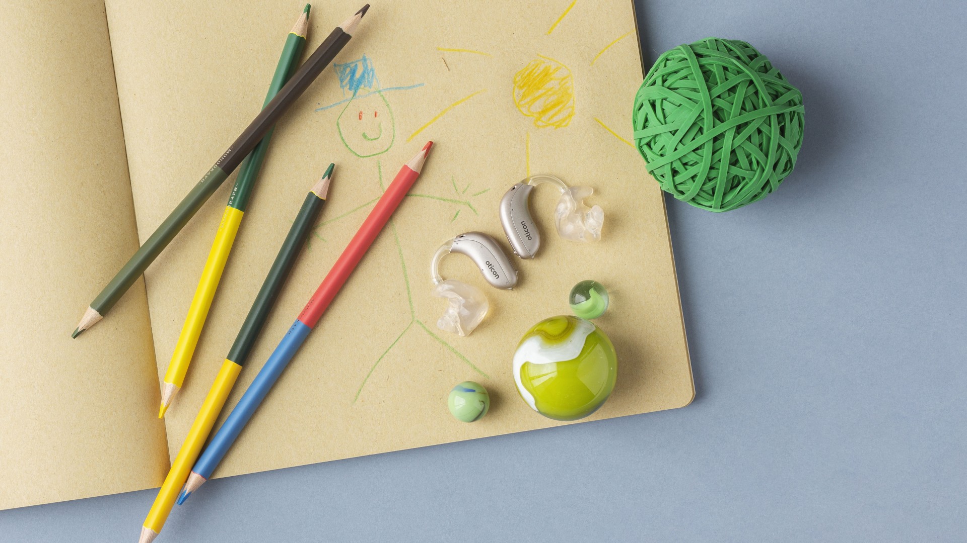 Kinderhörgeräte auf einer Zeichnung mit Buntstiften und Spielmaterial – kindgerechte Hörgeräteversorgung bei Hörgeräte Kersten für bestmögliches Hören, Sprachentwicklung und Lernen im Alltag.