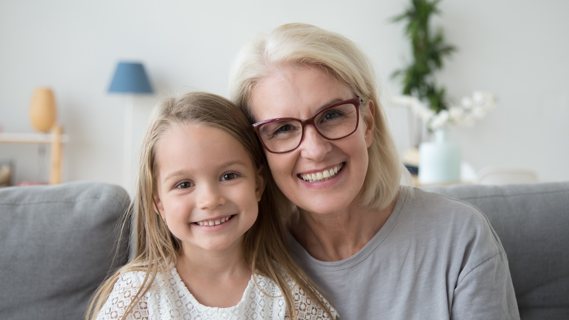 Glückliche Großmutter umarmt ihr Enkelkind auf dem Sofa – Lebensqualität, Nähe und unbeschwerte Familienmomente durch besseres Hören mit modernen Hörgeräten von Hörgeräte Kersten